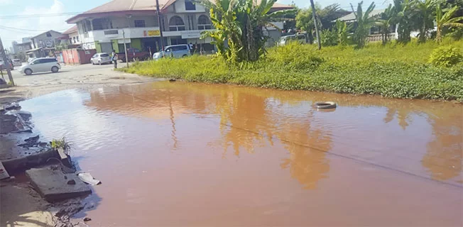 Grote waterplas op de hoek van de Surimomboweg en Coesewijnestraat na regenval in Suriname